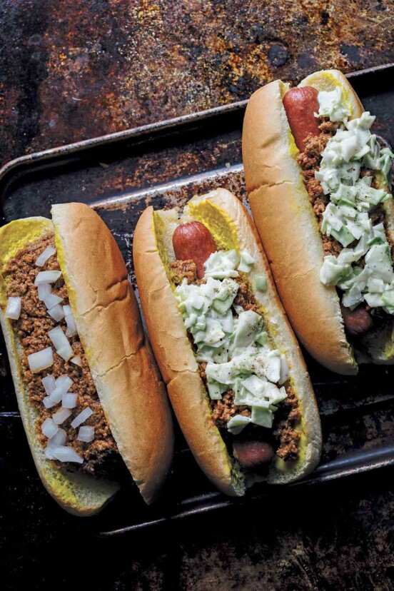 One chili bun and two slaw dogs on a rimmed baking sheet.