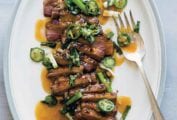 A white oval platter filled with sliced duck à l’orange, topped with sliced scallions and jalapenos, and drizzled with sauce.