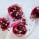 Four portions of roasted beet and quinoa salad served in a radicchio leaves on a white marble board.