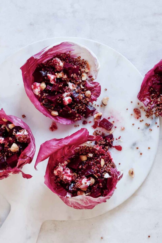 Four portions of roasted beet and quinoa salad served in a radicchio leaves on a white marble board.