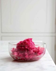 A glass bowl filled with Campari sorbet on a white marble countertop.
