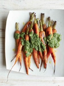 A white platter with nine roasted carrots covered in carrot top pesto.