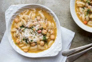 Two white bowls filled with chickpea and cavatelli soup on white napkin with spoons.