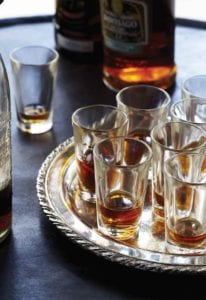 Several shot glasses partially filled with Cuba libre on a silver platter.