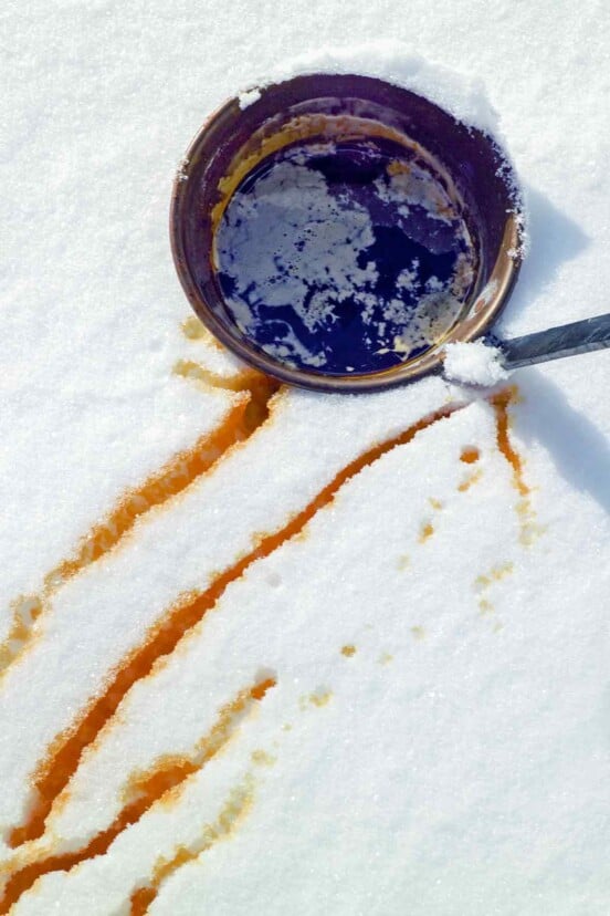 A bucket of maple syrup in the snow with streaks of maple syrup snow nearby