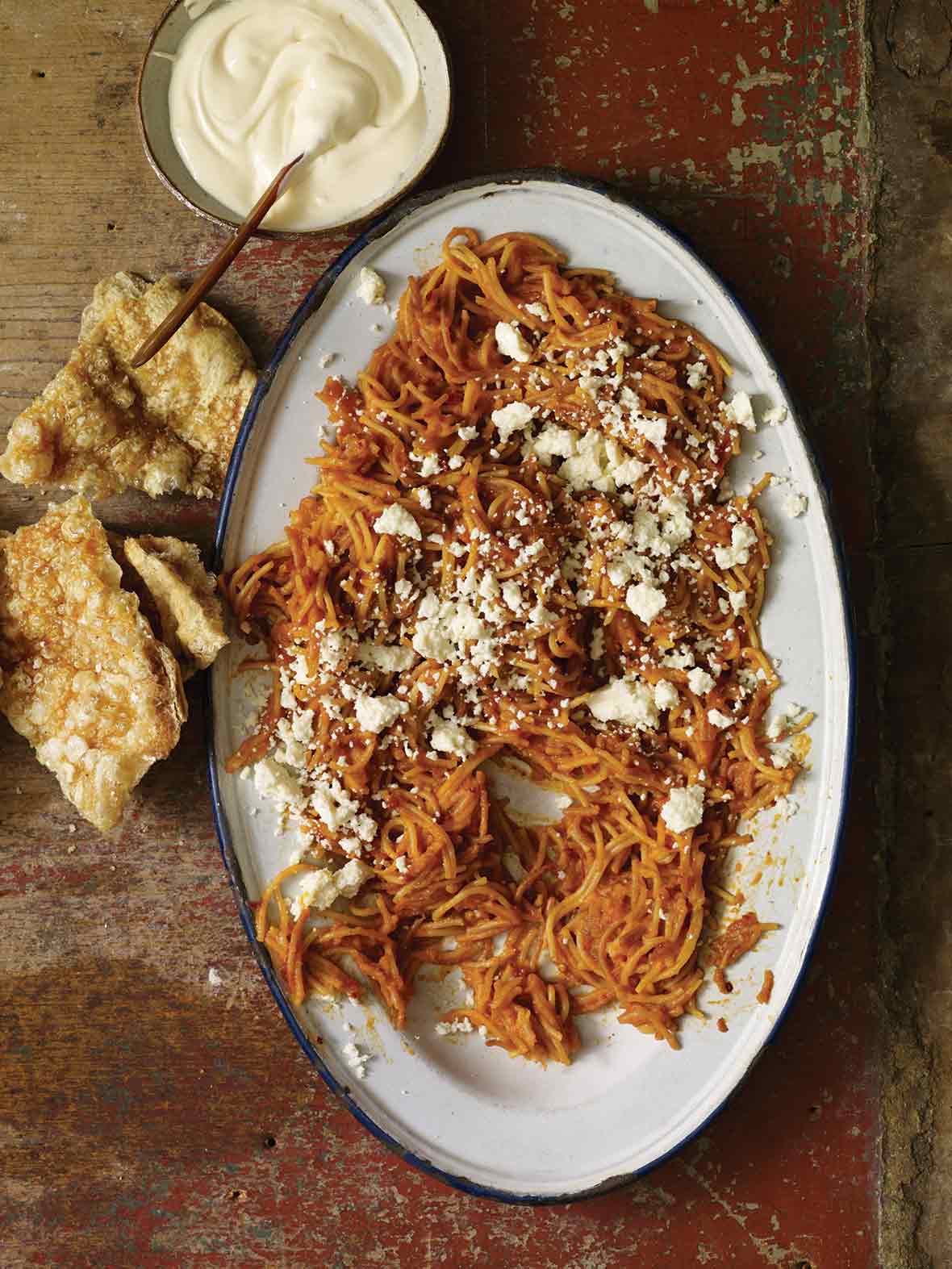 A platter of Mexican spaghetti with a bowl of crema on the side.