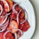A white plate filled with blood orange and red onion salad with a grinding of pepper on top.