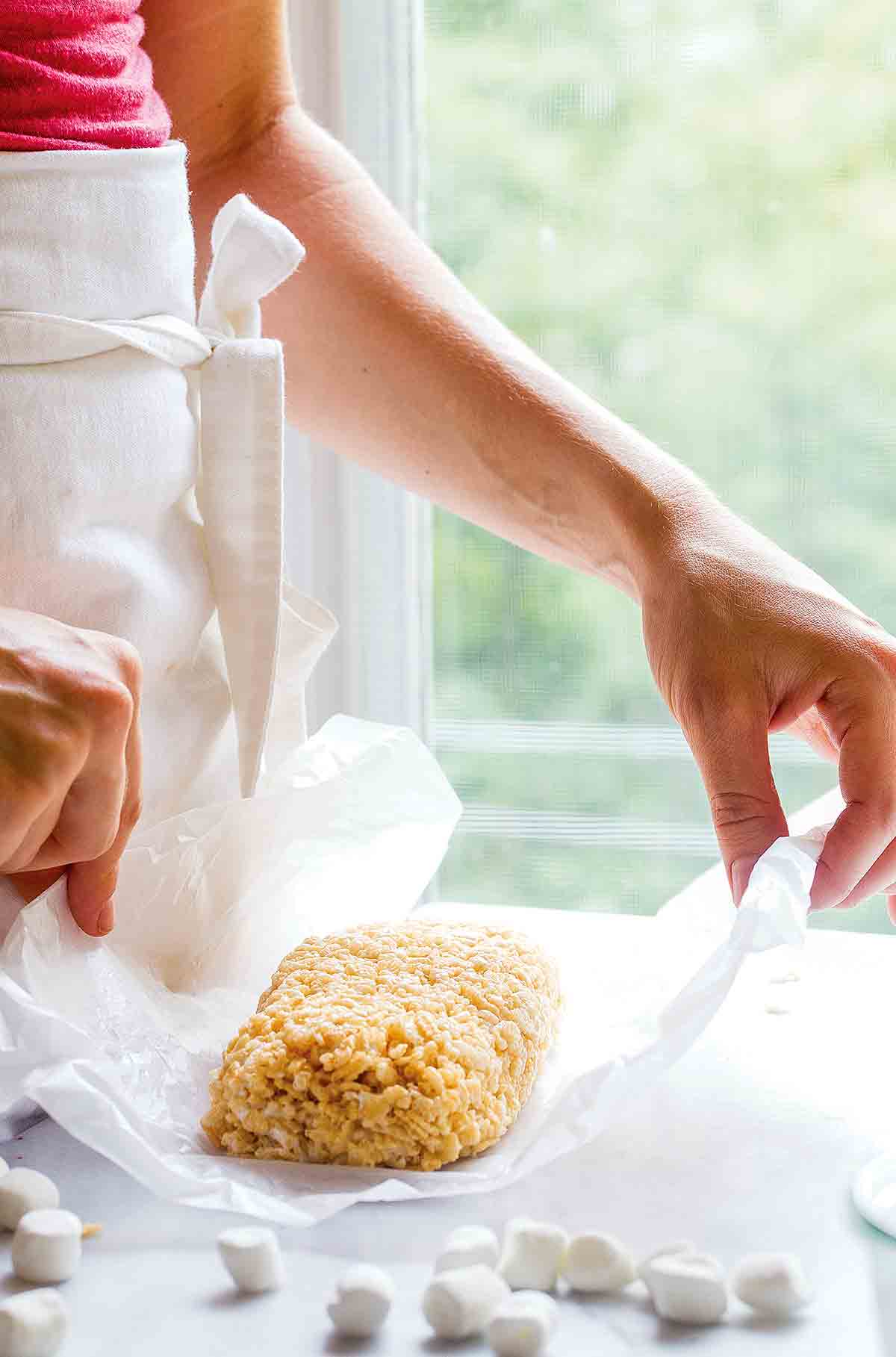 A woman holding a small batch of Rice Krispies treats for two on a piece of wax paper.