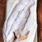 An entire fish baked in a salt crust on a baking sheet lined with parchment.
