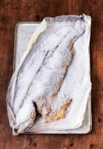 An entire fish baked in a salt crust on a baking sheet lined with parchment.