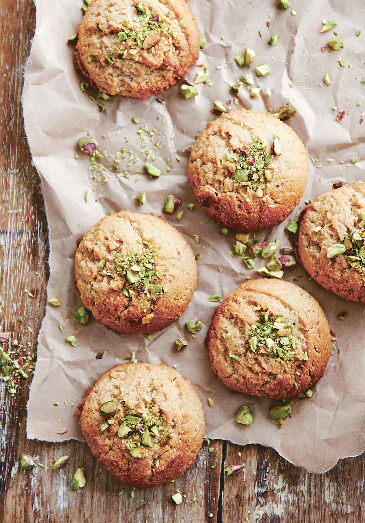 Six tahini cookies on a piece of parchment with chopped pistachios on the cookies and on the parchment.
