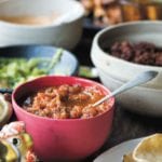 A red bowl filled with fire-roasted salsa in the middle of a Mexican feast.