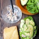 The makings of a Mediterranean tuna melt -- a slice of whole grain bread topped with gruyere cheese, a bowl with tuna salad, and a butter lettuce leaf topped with tuna salad, avocado, and pepper