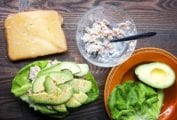 The makings of a Mediterranean tuna melt -- a slice of whole grain bread topped with gruyere cheese, a bowl with tuna salad, and a butter lettuce leaf topped with tuna salad, avocado, and pepper