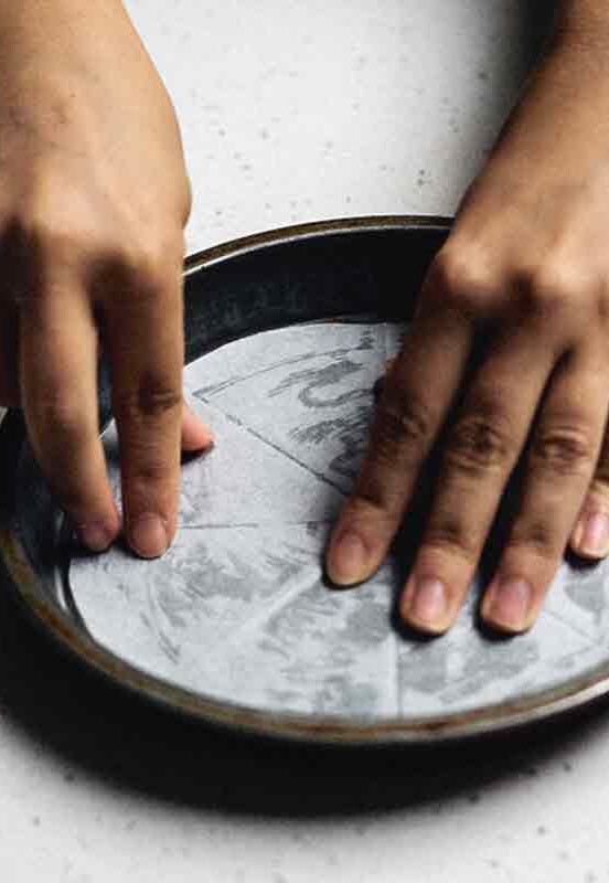 A person demonstrating how to line a pan with parchment paper by fitting a cut circle of paper into the pan.