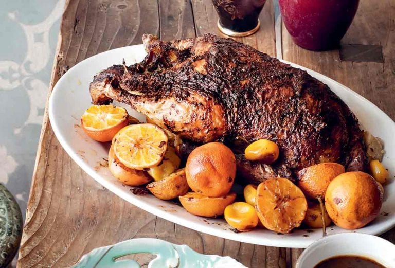 A white oval platter holding a whole roast duck with clementines scattered around it.