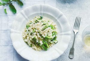 A plate and a bowl of asparagus risotto with a fork resting beside the bowl.