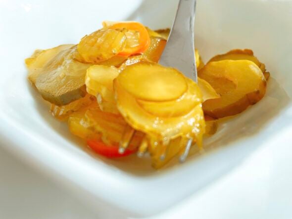 A white bowl with sliced barbecue pickles resting on a fork.