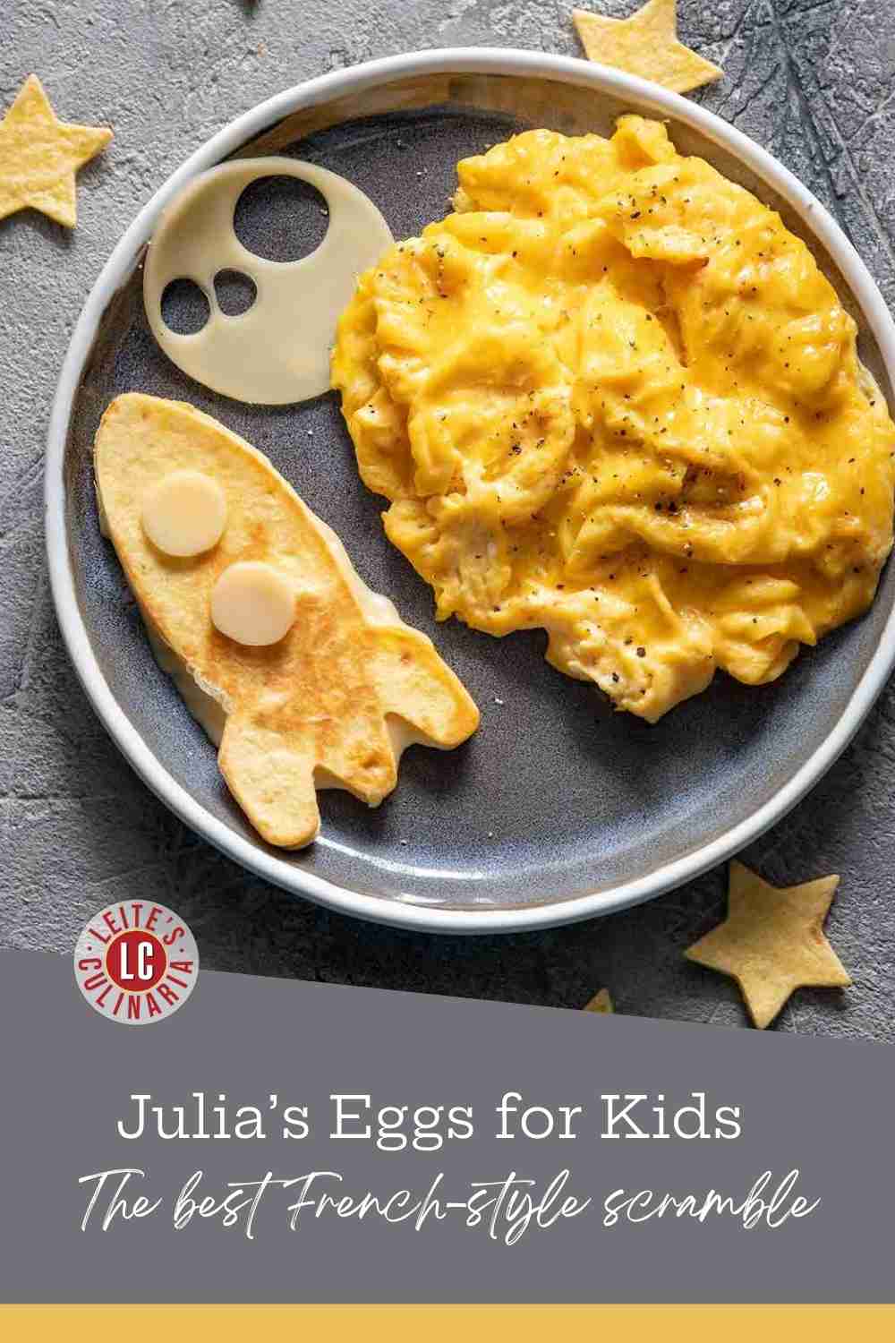 Creamy yellow scrambled eggs on a plate with a rocket-shaped pancake and pastry stars on a gray surface.