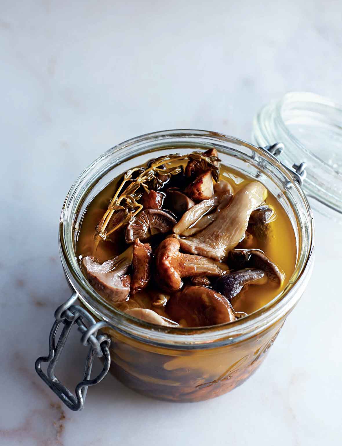 A canning jar filled with pickled wild mushrooms and a sprig of thyme.