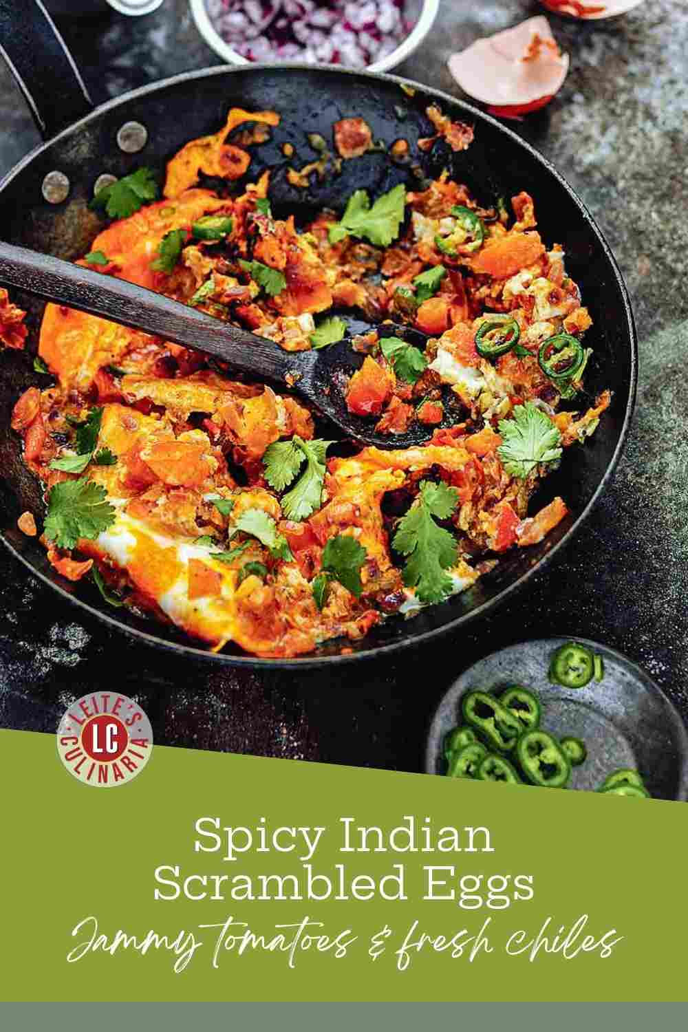 Spicy scrambled eggs in a cast iron skillet with cilantro, green chiles, and a wooden spoon.