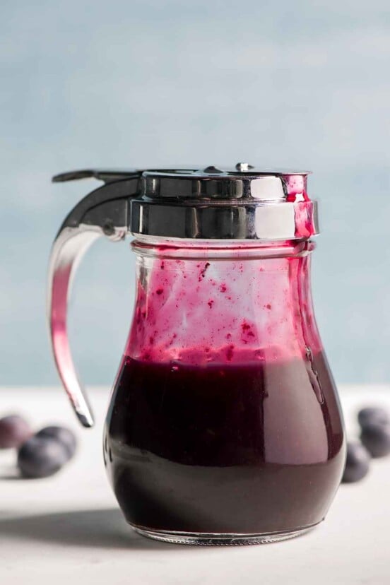 A diner-style dispenser half-filled with blueberry syrup.