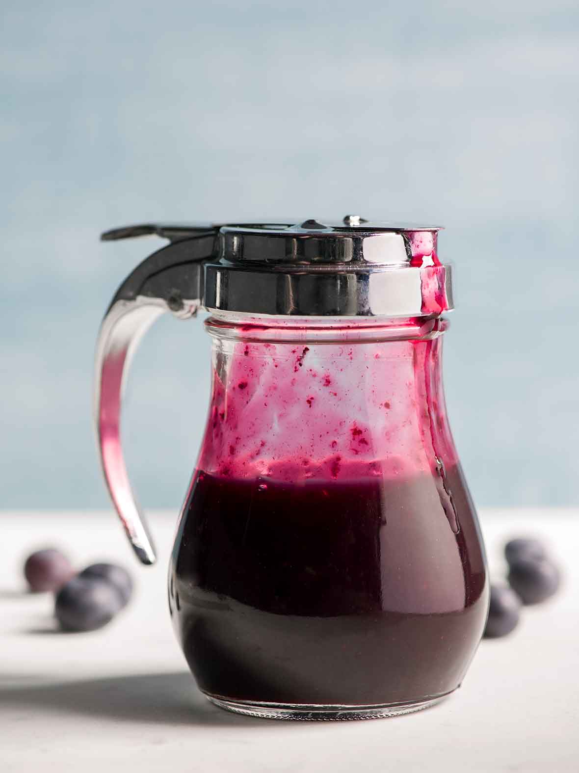 A diner-style dispenser half-filled with blueberry syrup.
