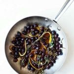 A skillet filled with black olives in an infusion of herbs and lemon and orange peel.