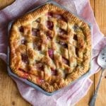 A hexagonal rhubarb pie with a lattice top crust on a pink linen cloth with a pie server resting beside the pie.