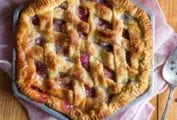 A hexagonal rhubarb pie with a lattice top crust on a pink linen cloth with a pie server resting beside the pie.