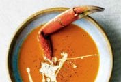 A bowl of creamy crab soup drizzled with cream, and sprinkled with pepper, with a crab leg sticking out of it.