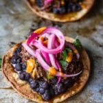 Two shredded beef tostadas topped with beans, beef, and pickled onions.