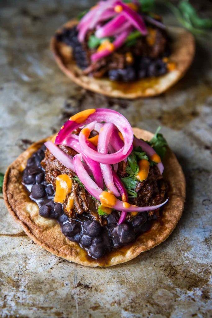 Two shredded beef tostadas topped with beans, beef, and pickled onions.