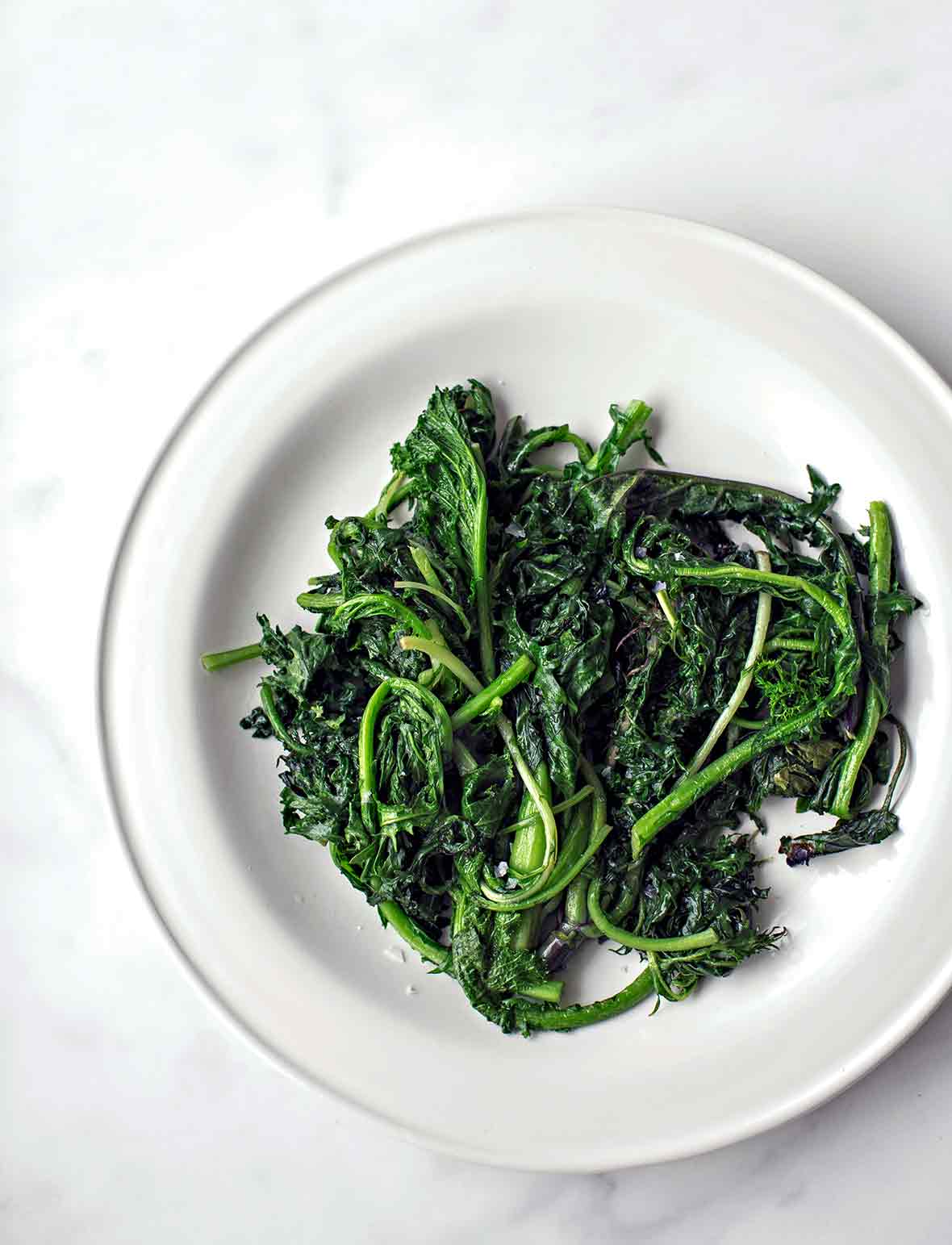 A pile of charred greens--kale and spinach--on a white plate.