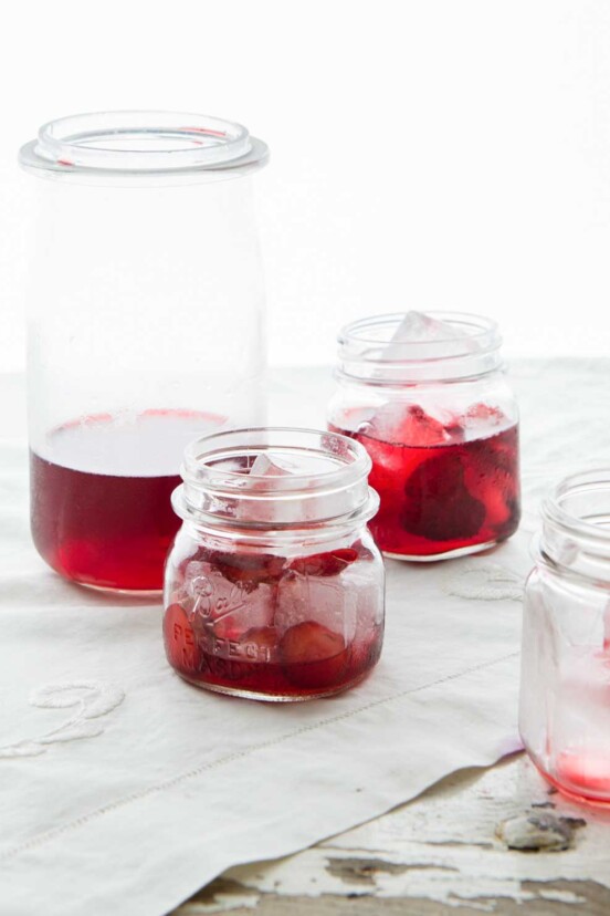 A tall bottle and several small jars filled with strawberry punch and ice cubes.