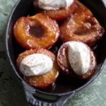 Baked nectarines with Port in a cast-iron casserole dish, three nectarines topped with whipped cream and grated nutmeg.