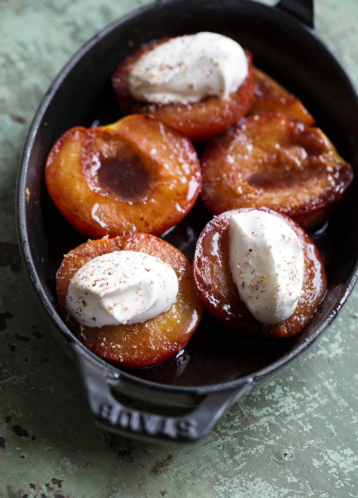 Baked nectarines with Port in a cast-iron casserole dish, three nectarines topped with whipped cream and grated nutmeg.