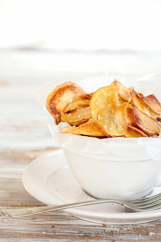 A white bowl filled with salt and vinegar potato chips with a fork resting beside.
