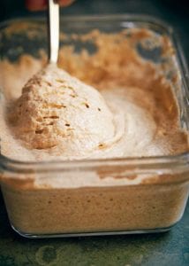 A glass container of sourdough starter with a spoon.