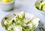 Two white bowls filled with shaved zucchini salad, topped with dill sprigs and two forks on the side.