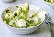 Two white bowls filled with shaved zucchini salad, topped with dill sprigs and two forks on the side.