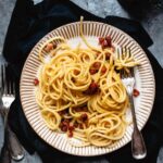 En skål fylld med spaghetti carbonara, toppad med nyriven parmesan.