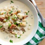 Steamer clam chowder on a green gingham napkins with a spoon nearby.