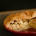 An apple pie with Cheddar crust in a red pie pan cut into to show the Golden Delicious apples inside