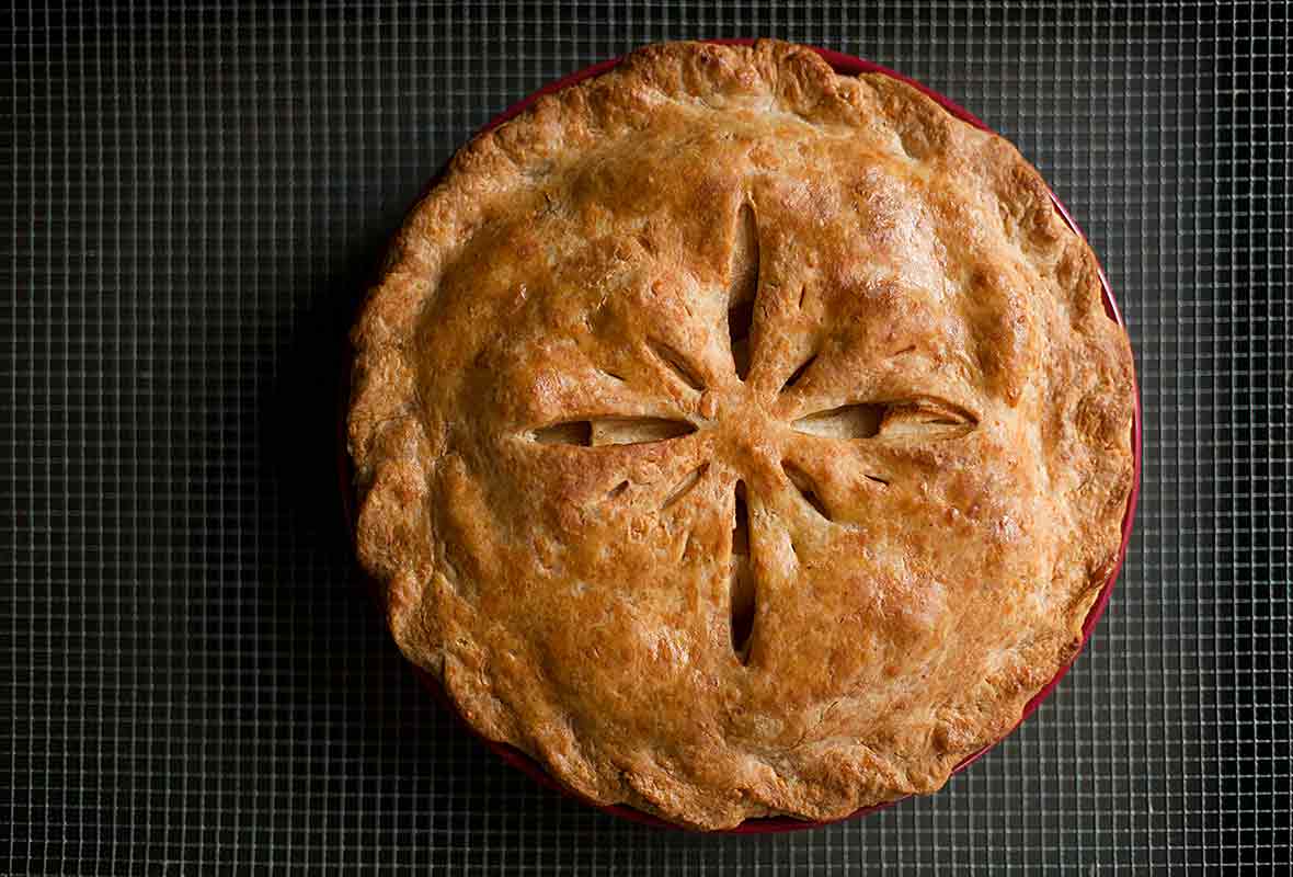 An apple pie with a Cheddar crust in a red pie pan cut into to show the Golden Delicious apples inside.