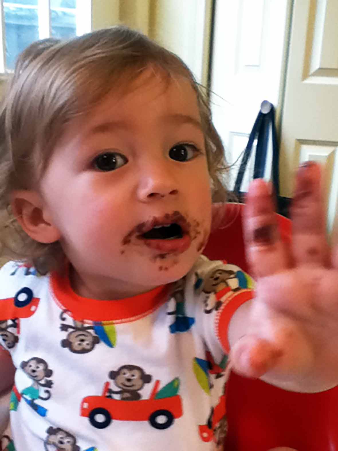 An toddler proudly showing his face smeared with Nutella