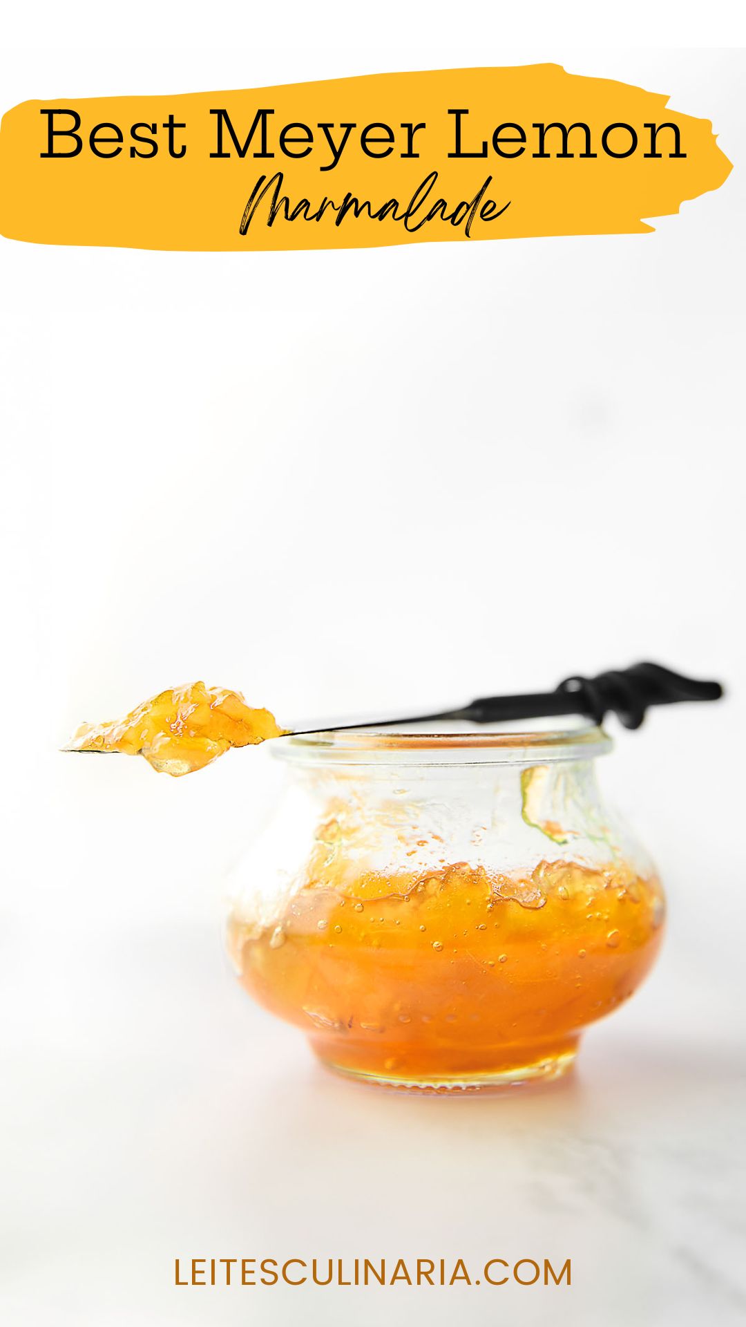 A small jam jar filled with Meyer lemon marmalade. Resting on top is a knife with a dollop of marmalade on top.