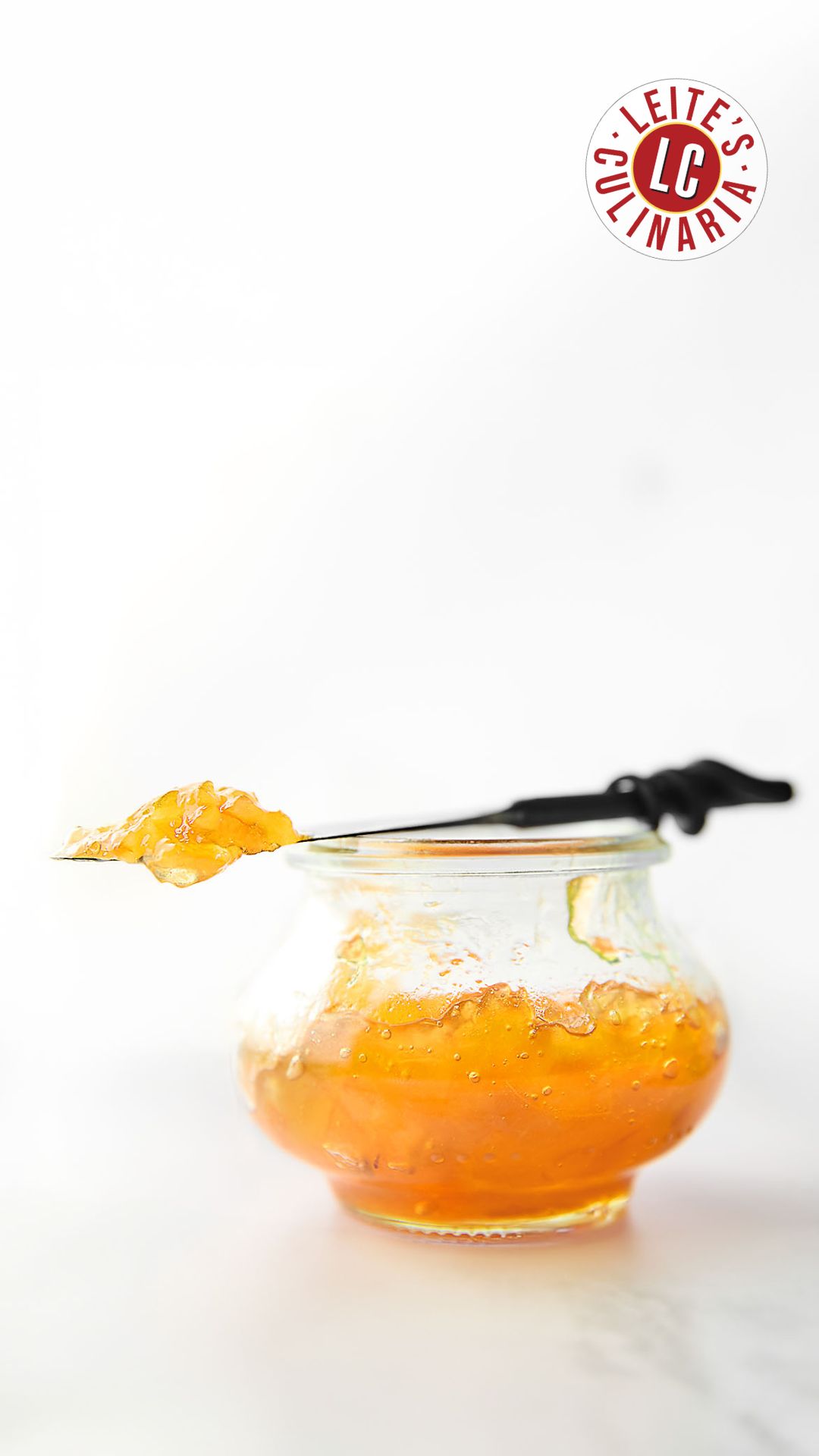 A small jam jar filled with Meyer lemon marmalade. Resting on top is a knife with a dollop of marmalade on top.