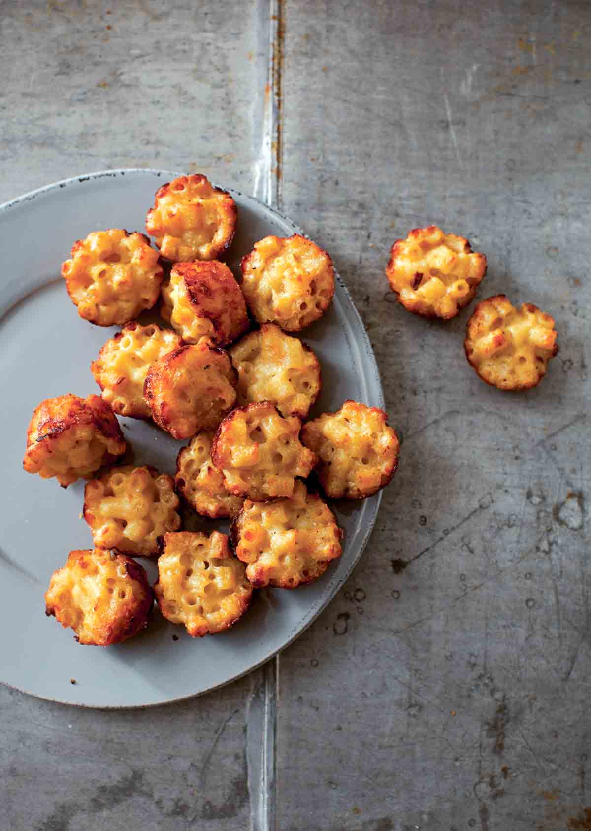 A grey plate half-filled with mac and cheese canapes, with a few resting beside the plate