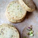 Five round pistachio shortbread cookies with a few broken pistachios on the side.